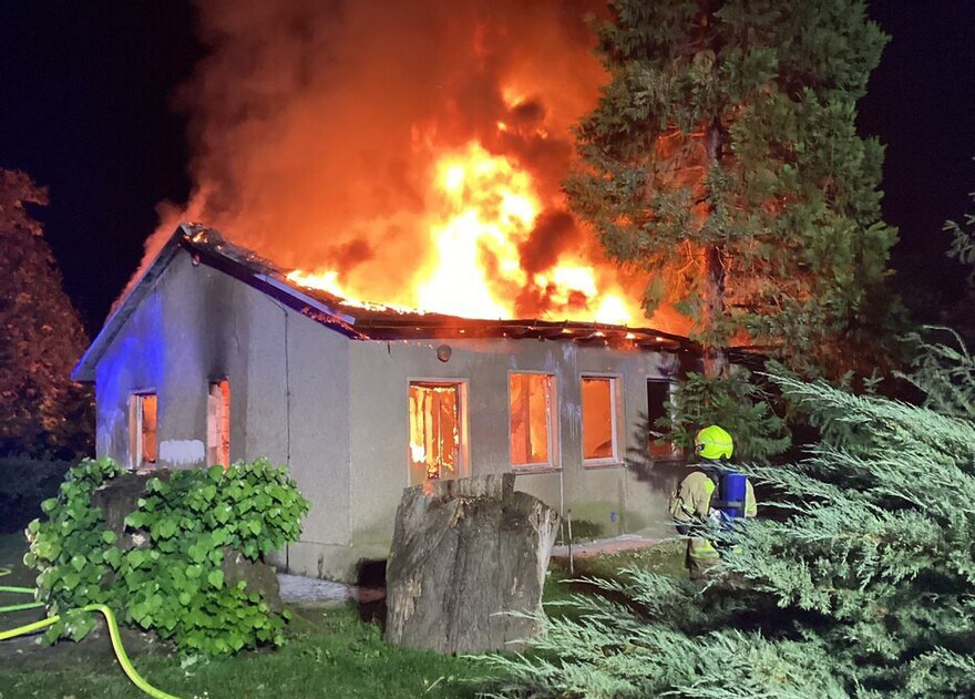 Ein kleines Haus steht in Flammen. Die Feuerwehr löscht den Brand.