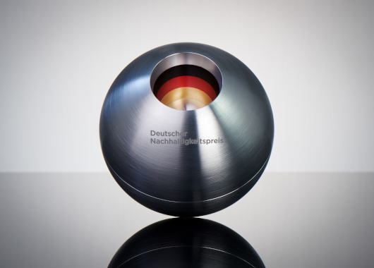 Eine silberne Metallkugel mit einer Einbuchtung in der Mitte in den Farben schwarz, rot, gold und der Aufschrift Deutscher Nachhaltigkeitspreis.