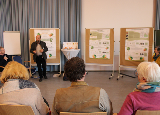 Mehrere Menschen sitzen im Halbkreis auf einen Referenten ausgerichtet