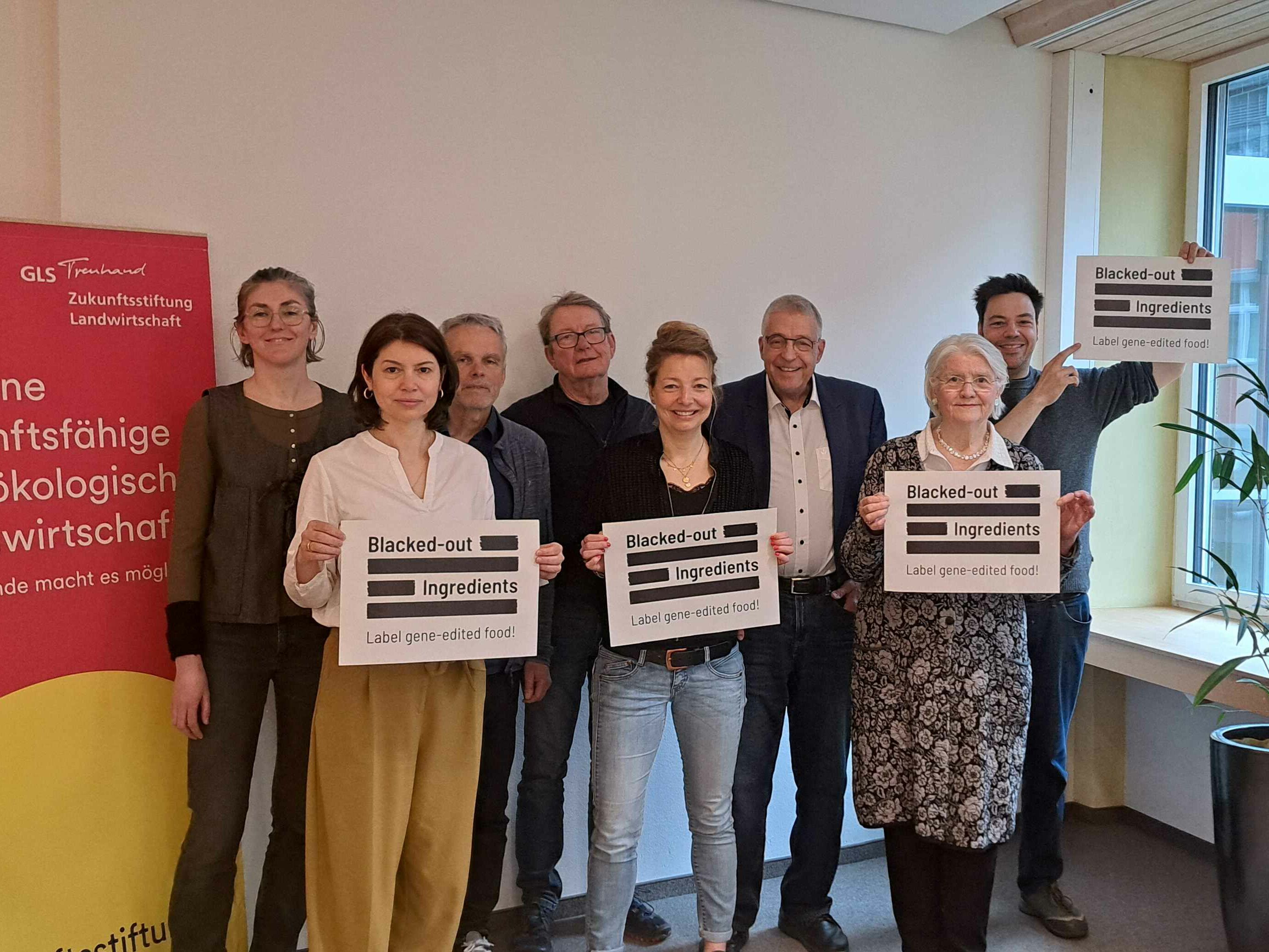 Acht Menschen halten Plakate mit der Aufschrift Blecked-out Ingredients hoch.