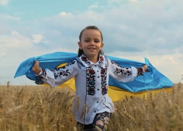Mädchen läuft mit der ukrainischen Flagge über ein Getreidefeld