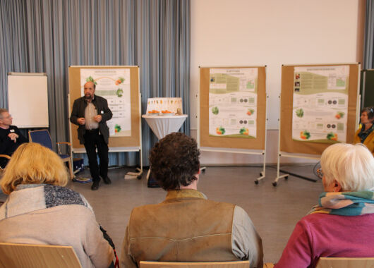 Mehrere Menschen sitzen im Halbkreis auf einen Referenten ausgerichtet